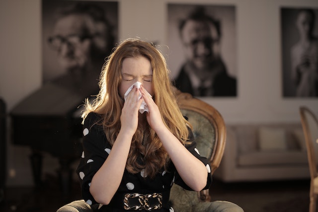 Person with long red hair sitting down and blowing their nose into a tissue